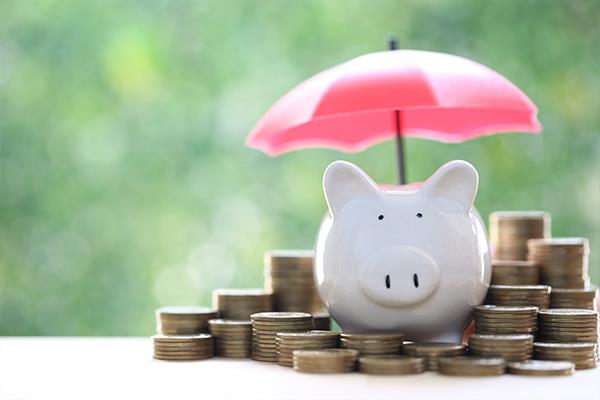 Piggy bank sat on top of a pile of coins underneath an umbrella