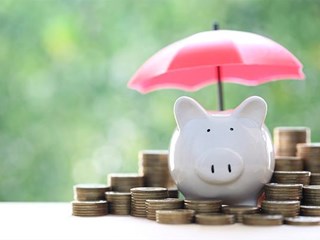 Piggy bank sat on top of a pile of coins underneath an umbrella