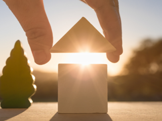 Hand putting the roof on a wooden house