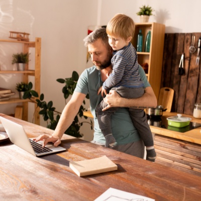 a father holding his son in his arms whilst on the laptop