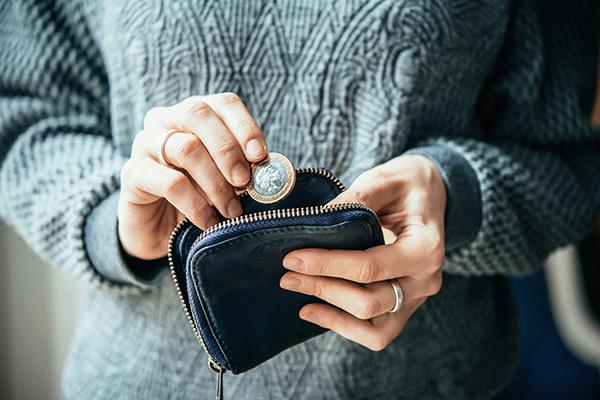 A hand depositing a pound coin into a purse.