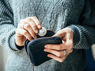 A hand depositing a pound coin into a purse.