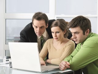 two men and one woman looking at a laptop