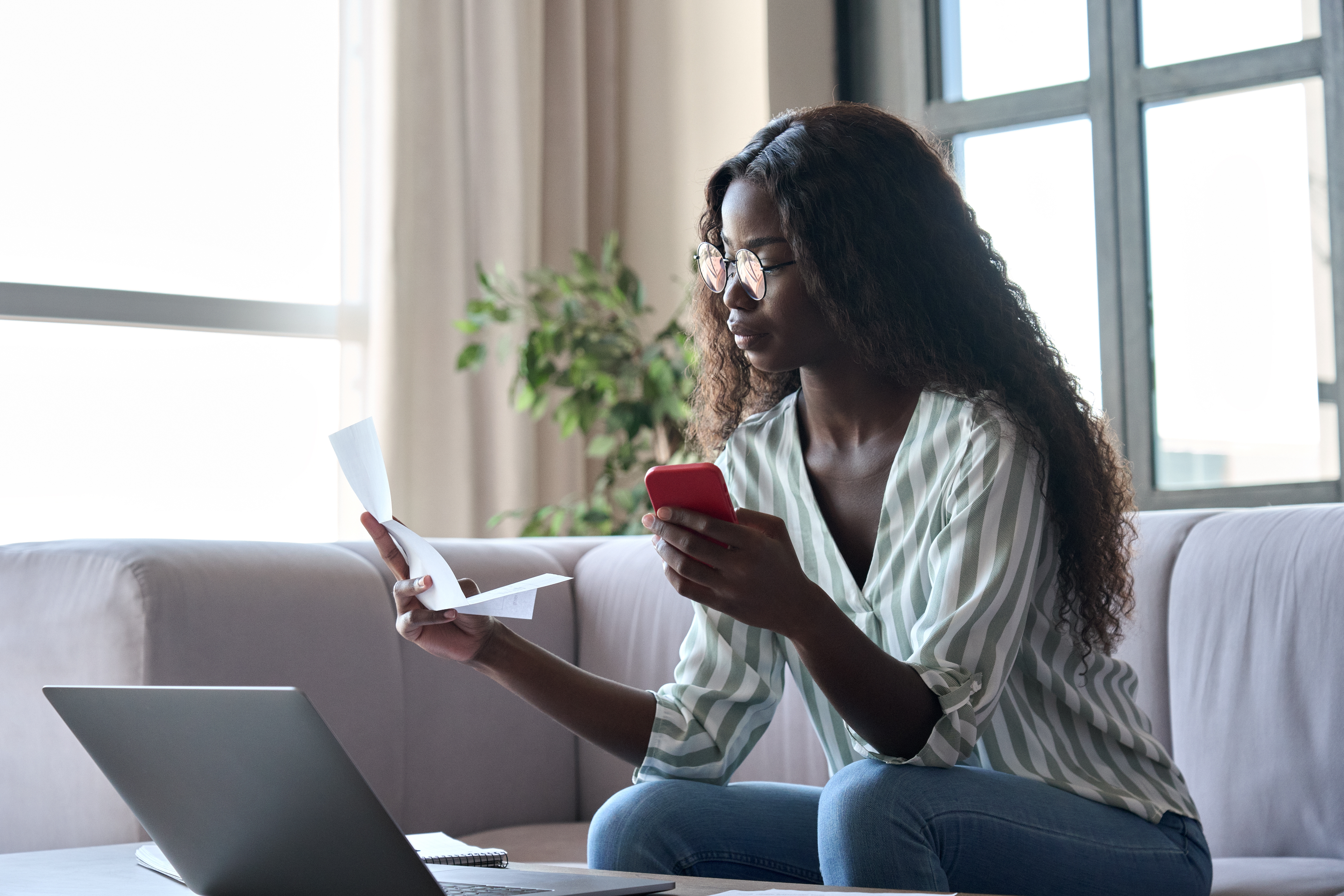 Woman reviewing paperwork with phone and laptop