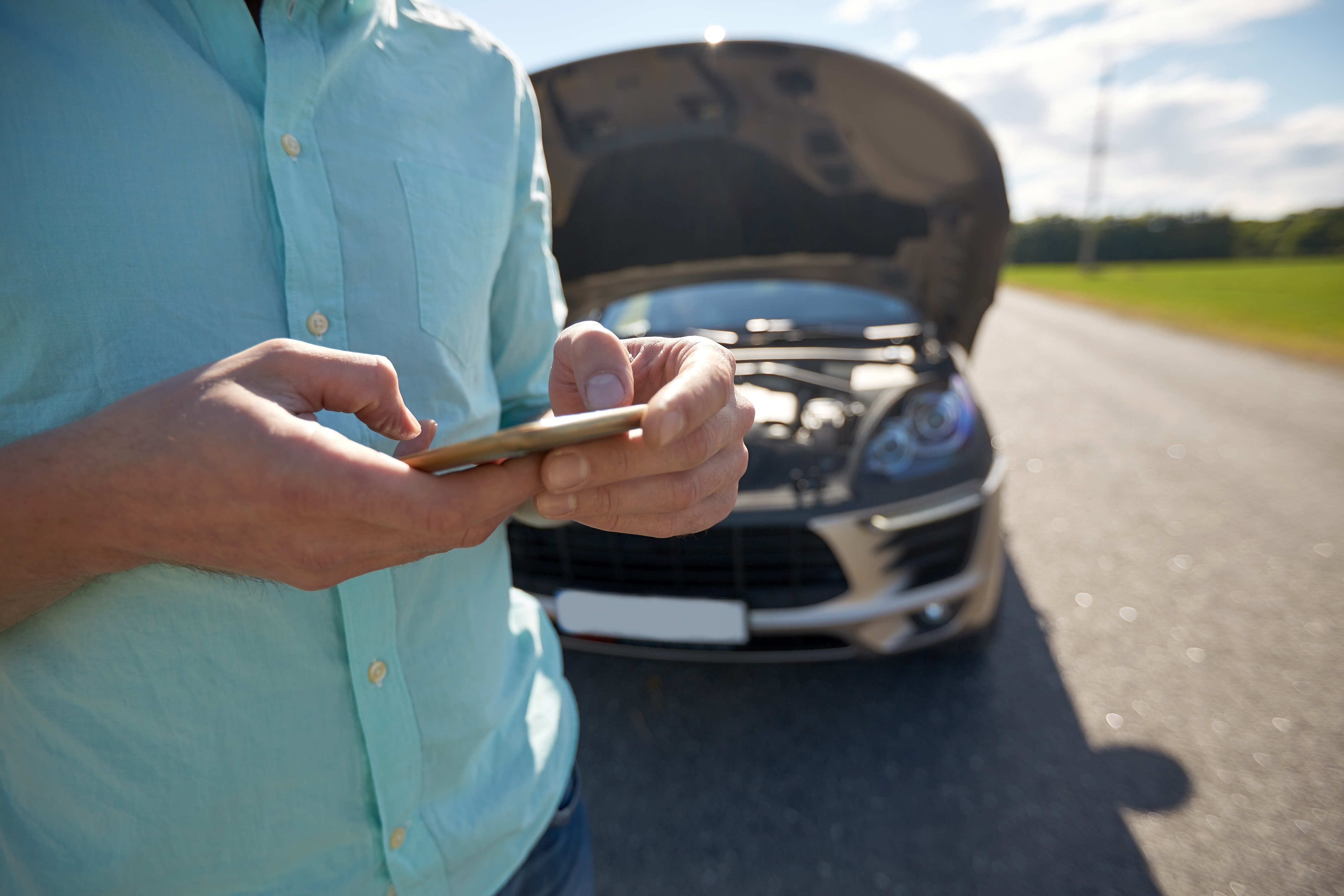 a person making a telephone call with a broken down car behind them