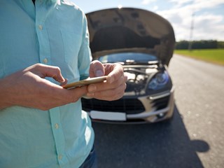 a person making a telephone call with a broken down car behind them