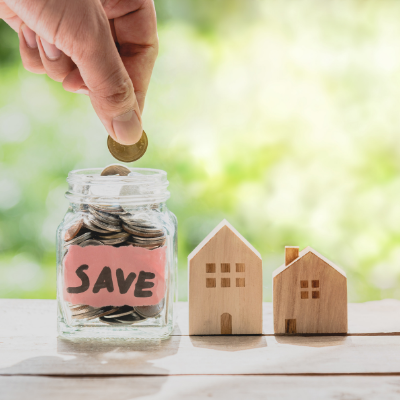 person placing coins in a jar with two wooden houses beside it
