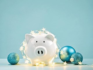 A piggy bank wrapped in Christmas lights and surrounded by baubles.