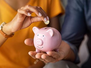 People depositing a pound coin in a piggy bank