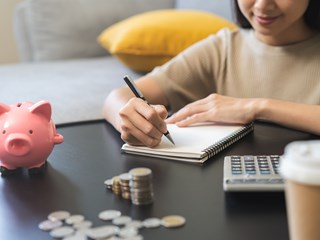 Woman counting savings, coin stacks, calculator and piggy bank