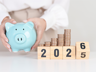 Piggy bank next to wooden block spelling 2025 and 2026 with coin stacks on top.