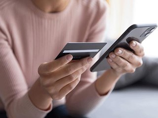Person holding a bank card in one hand and a mobile phone in the other.