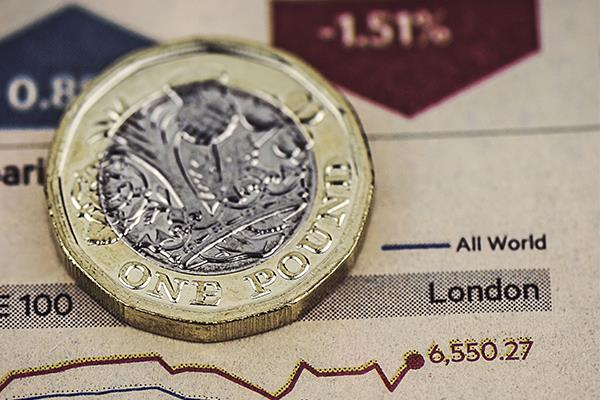 Pound coin on top of graph tracking stocks performance.