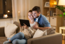 a couple sitting on the sofa, both looking at their tablet device
