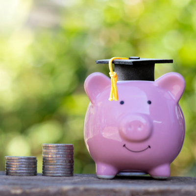 a piggybank wearing a graduation hat with coins stacked next to it