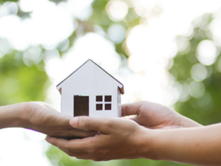 two pairs of hands holding a small house