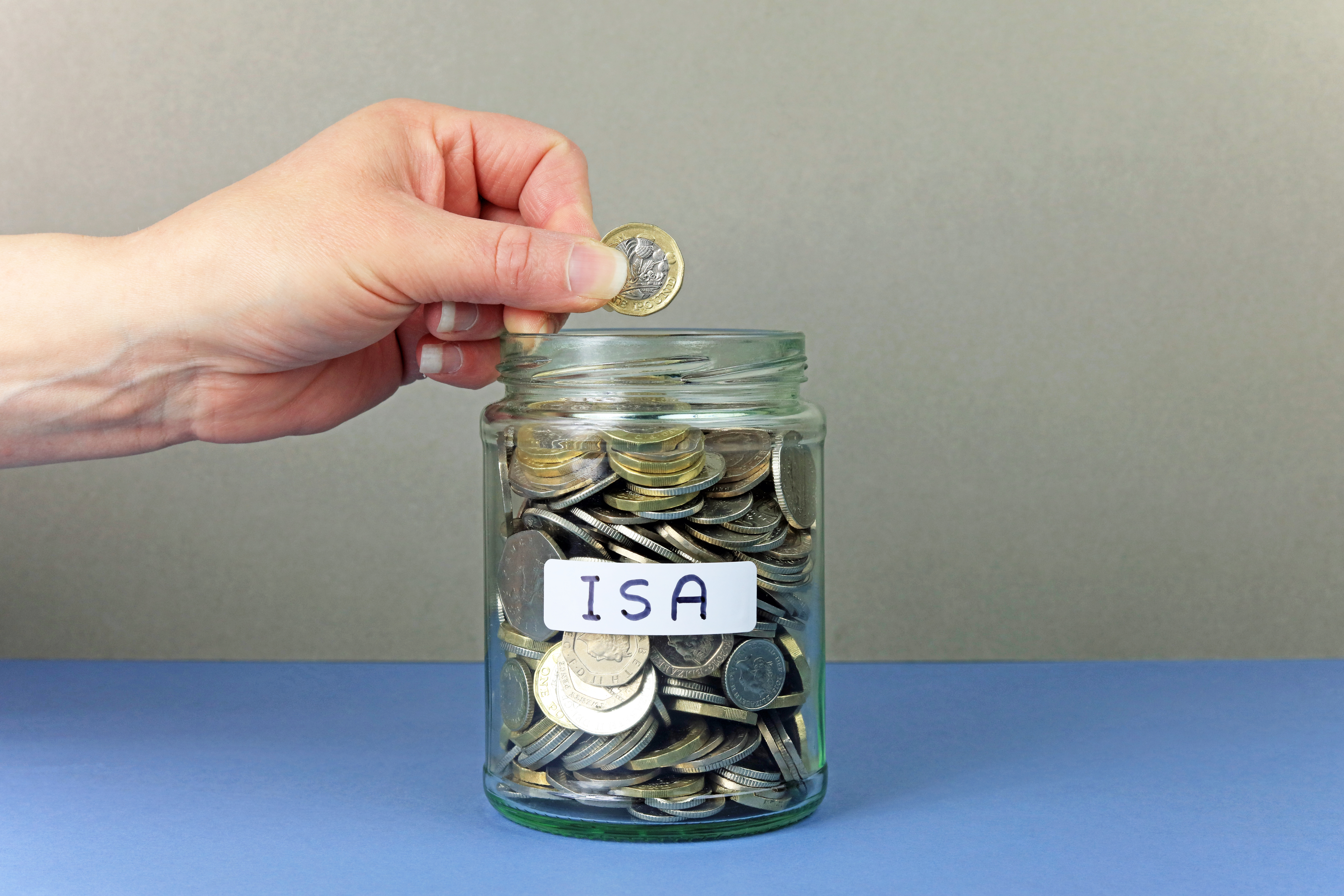 Hand depositing coin into a jar of savings labelled 'ISA'