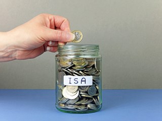 Hand depositing coin into a jar of savings labelled 'ISA'