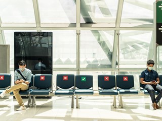 two people sitting on chairs at an airport while social distancing and wearing masks