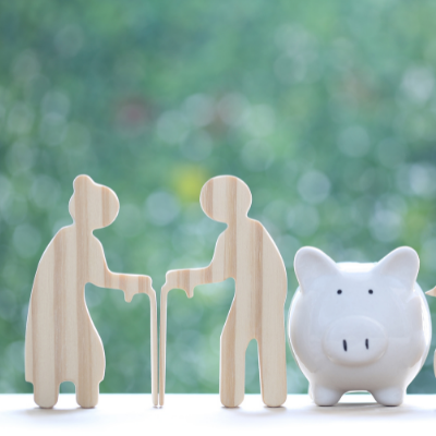 wooden cut outs of elderly couple beside a white piggy bank