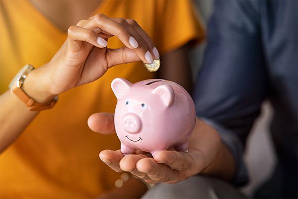 Person depositing pound coin in piggy bank