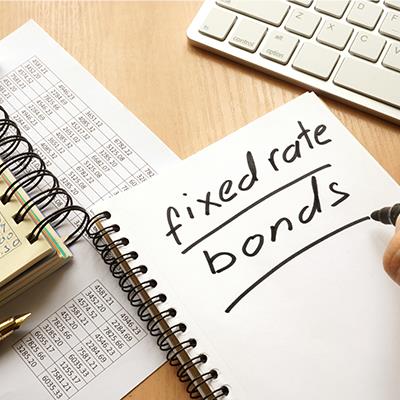The words 'fixed rate bonds' written on a notebook, sat on a table next to a laptop and list of numbers.