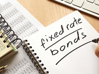 The words 'fixed rate bonds' written on a notebook, sat on a table next to a laptop and list of numbers.