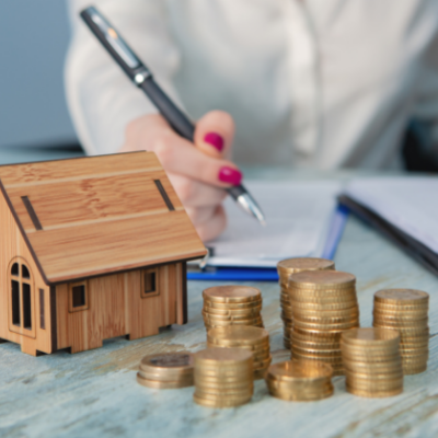 Person completing mortgage application, a toy house and coin stacks.
