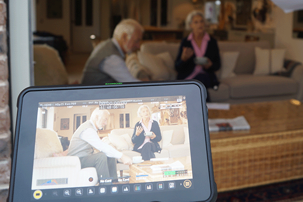 Image of a camera lens focusing on a couple sat on a sofa.