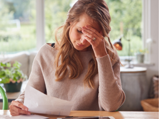woman holding her head whilst looking at paperwork
