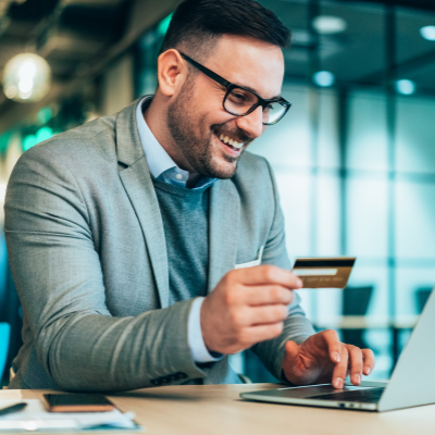 A man in glasses holding a credit card whilst working on a laptop