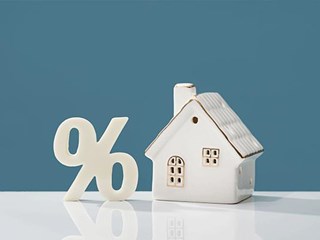 Small, ceramic house next to a percentage symbol on top of a table.