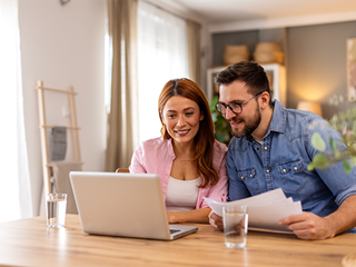 Couple with paperwork looking at a laptop.