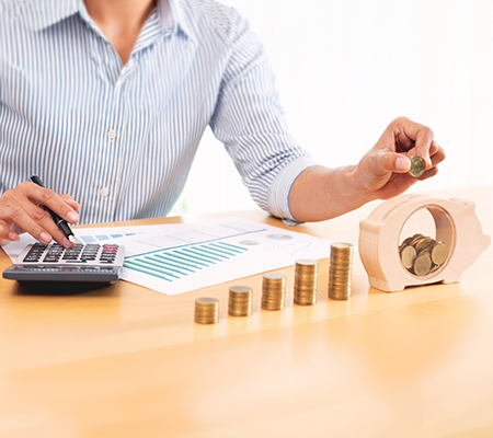 Woman placing coin in piggy bank next to coin stacks