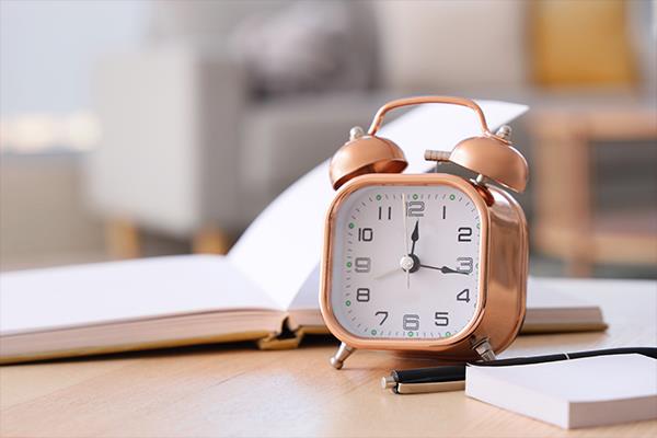 Alarm clock on a desk with a notebook and pen.