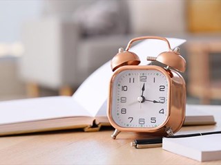 Alarm clock on a desk with a notebook and pen.